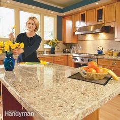 a woman standing in a kitchen next to a counter with flowers and fruit on it