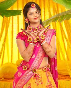 a woman in a yellow and pink sari with flowers on her chest, posing for the camera