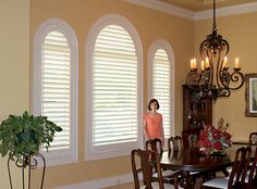 a woman standing in front of a dining room table with chairs and a chandelier