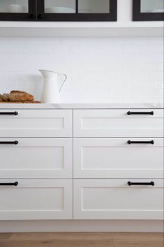 a kitchen with white cabinets and black handles on the countertop, along with bread