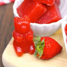 some strawberries are sitting on a cutting board next to a bowl of jelly bears