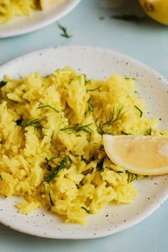 a white plate topped with yellow rice and lemon wedges next to two plates of food