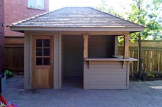 a small wooden gazebo in the middle of a brick patio next to a fence