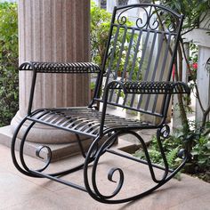 a black rocking chair sitting on top of a stone floor next to a planter