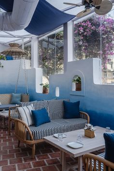 an outdoor seating area with blue and white striped couches, tables and hanging plants