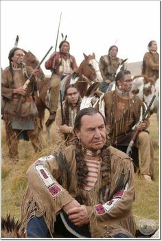 a group of men dressed in native american clothing sitting on the ground next to each other