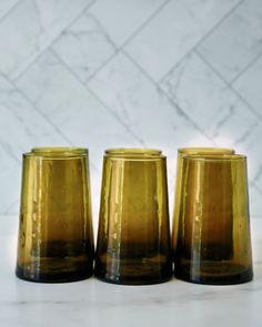 three yellow glass cups sitting next to each other on a white counter top in front of a marble wall