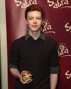 a man standing in front of a red wall holding an apple