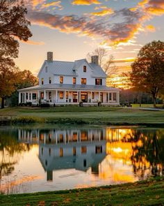 a large white house sitting on top of a lush green field next to a lake