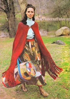 a woman wearing a red shawl is standing in the grass with her handbag