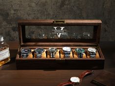 a wooden box with six watches in it and a bottle of whiskey next to it