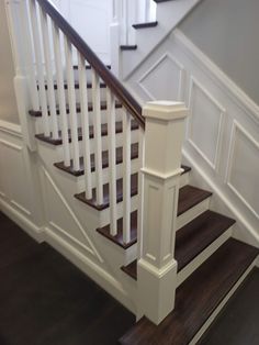 a white staircase with wooden handrails and dark wood flooring