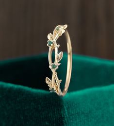 a gold ring with leaves on it sitting on top of a green velvet cloth in front of a wooden background