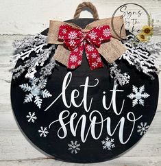 a sign that says let it snow on the side of a wooden board with red and white bows