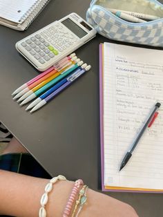 a person's hand with a pen, calculator and notebook on a table