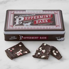 peppermint bark chocolates in a tin on a marble countertop next to two pieces of peppermint bark