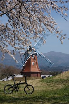 a bicycle parked next to a windmill on top of a grass covered field with trees in the background