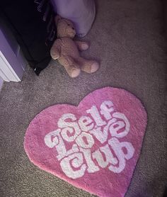 a pink heart shaped rug with the words self love club on it next to a teddy bear