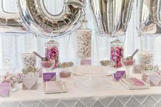 a table topped with lots of candy and confetti next to giant silver balloons