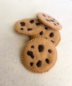 three cookies with chocolate chips on them sitting on top of a white tablecloth covered surface