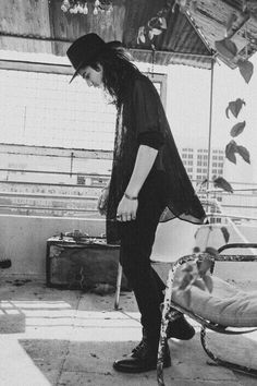 a man with long hair standing next to a bed