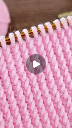 a pink knitted blanket with gold pins on the side and a video play button