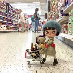 a doll is pushing a shopping cart with teddy bears in it at the grocery store