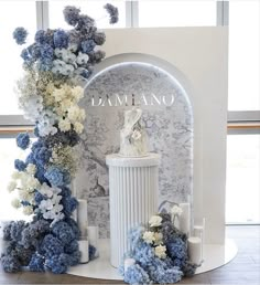 a white and blue wedding cake on top of a pedestal in front of a floral arch