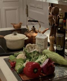 various vegetables are on a cutting board in the middle of a kitchen counter with wine bottles and other cooking utensils