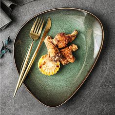 a green plate topped with meat and fruit next to a gold fork on top of a table