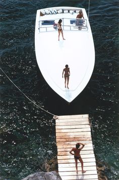 two people are standing on the dock next to a boat that is docked in the water