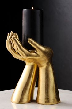 a gold hand holding a black candle holder