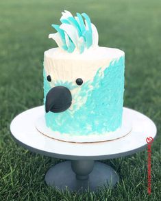 a blue and white cake with a bird decoration on it's face sitting in the grass