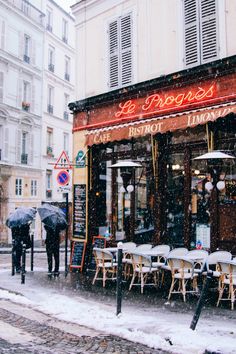 people are walking in the snow near an outdoor restaurant with tables and chairs covered by umbrellas