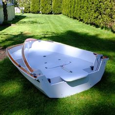 a white boat sitting on top of a lush green field next to a hedge covered yard