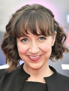 a close up of a person wearing a black dress and smiling at the camera with her hair pulled back