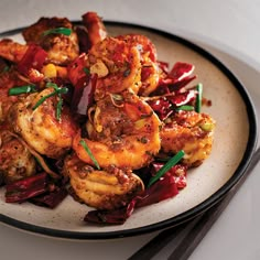 a white plate topped with cooked shrimp and veggies next to chopsticks