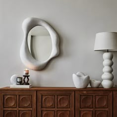 a white sculpture sitting on top of a wooden dresser next to a lamp and mirror