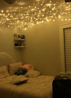 there is a bed with lights hanging from the ceiling and a laptop on top of it