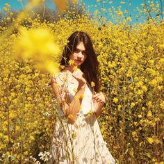 a woman standing in a field of yellow flowers with her hands on her chest and looking at the camera