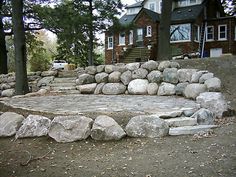 there is a rock wall and steps in front of the house with trees around it