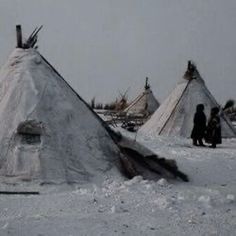 two people standing in front of teepees with snow on the ground