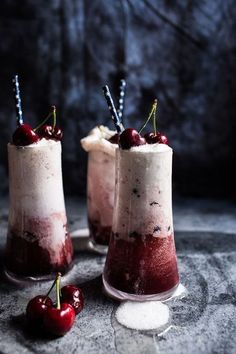 two glasses filled with ice cream and cherries on top of a stone table next to each other