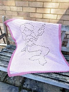 a pink and white crocheted blanket sitting on top of a wooden bench next to a brick wall