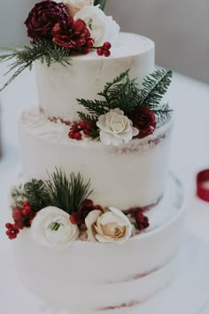 a three tiered white cake with red and white flowers on it's side