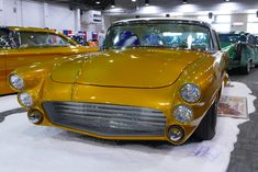 an old yellow car is on display in a showroom with other cars behind it