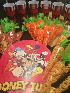 there are many snacks on the table with plastic cups in front of them, including carrots and noodles