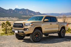 a tan toyota truck parked in the middle of a dirt road with mountains in the background