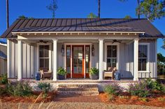 a small white house with porches and columns on the front door is surrounded by greenery