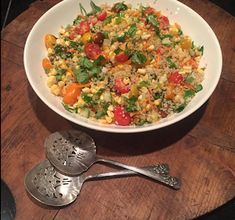 a white bowl filled with rice and vegetables next to two spoons